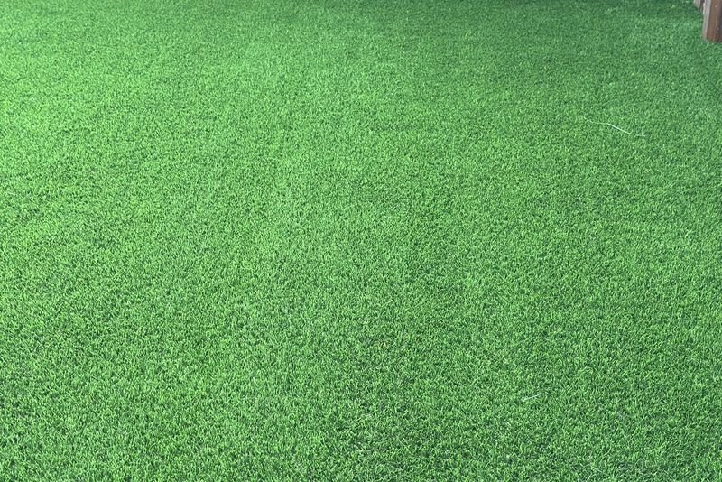 Primer plano de la fibra de grama artificial: hebras verdes de dos tonos mezcladas con hilo seco marrón.