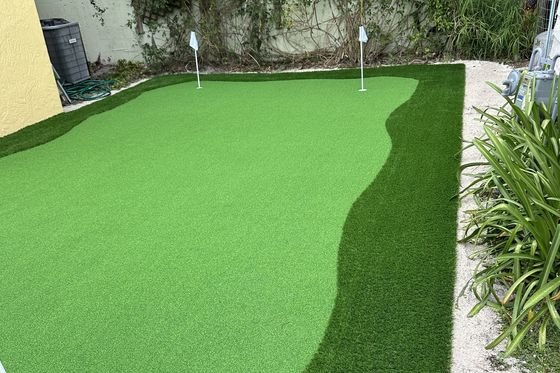 Putting green de grama artificial con dos banderas, delante de un muro cubierto de enredadera.