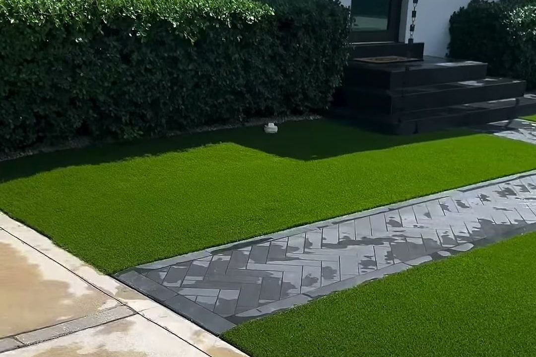 El mismo jardín delantero con grama artificial verde y pareja a ambos lados del camino.